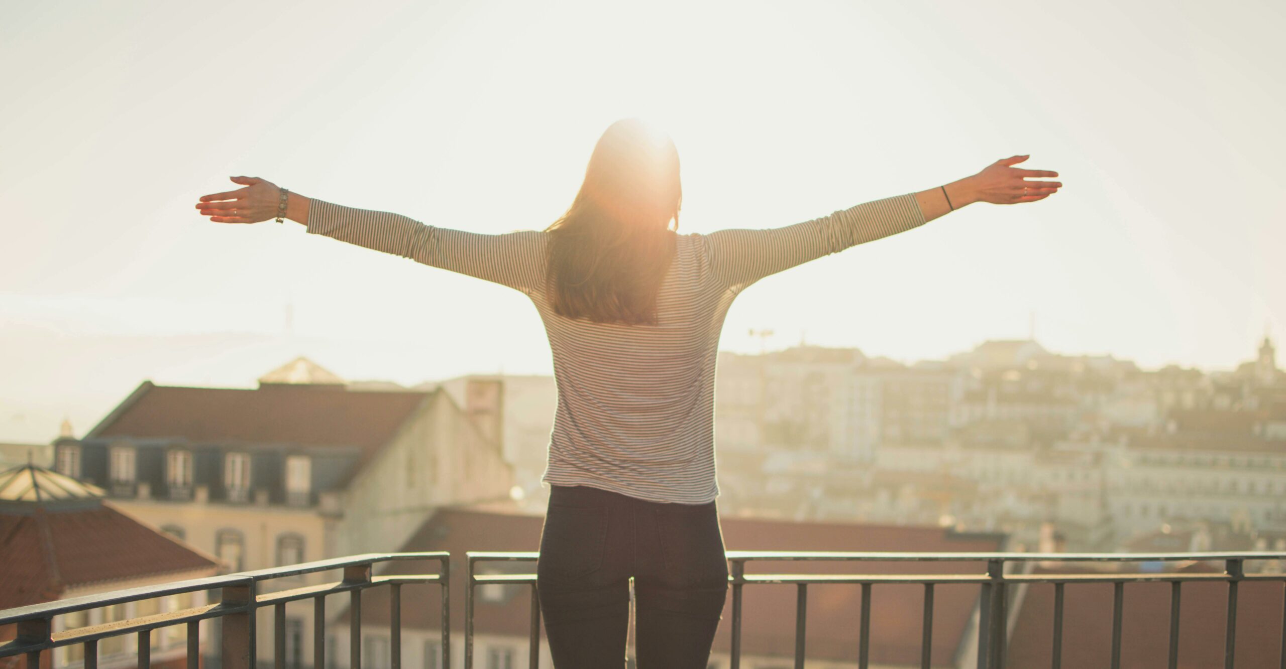 Woman standing outside in the sun with her arms outstretched.