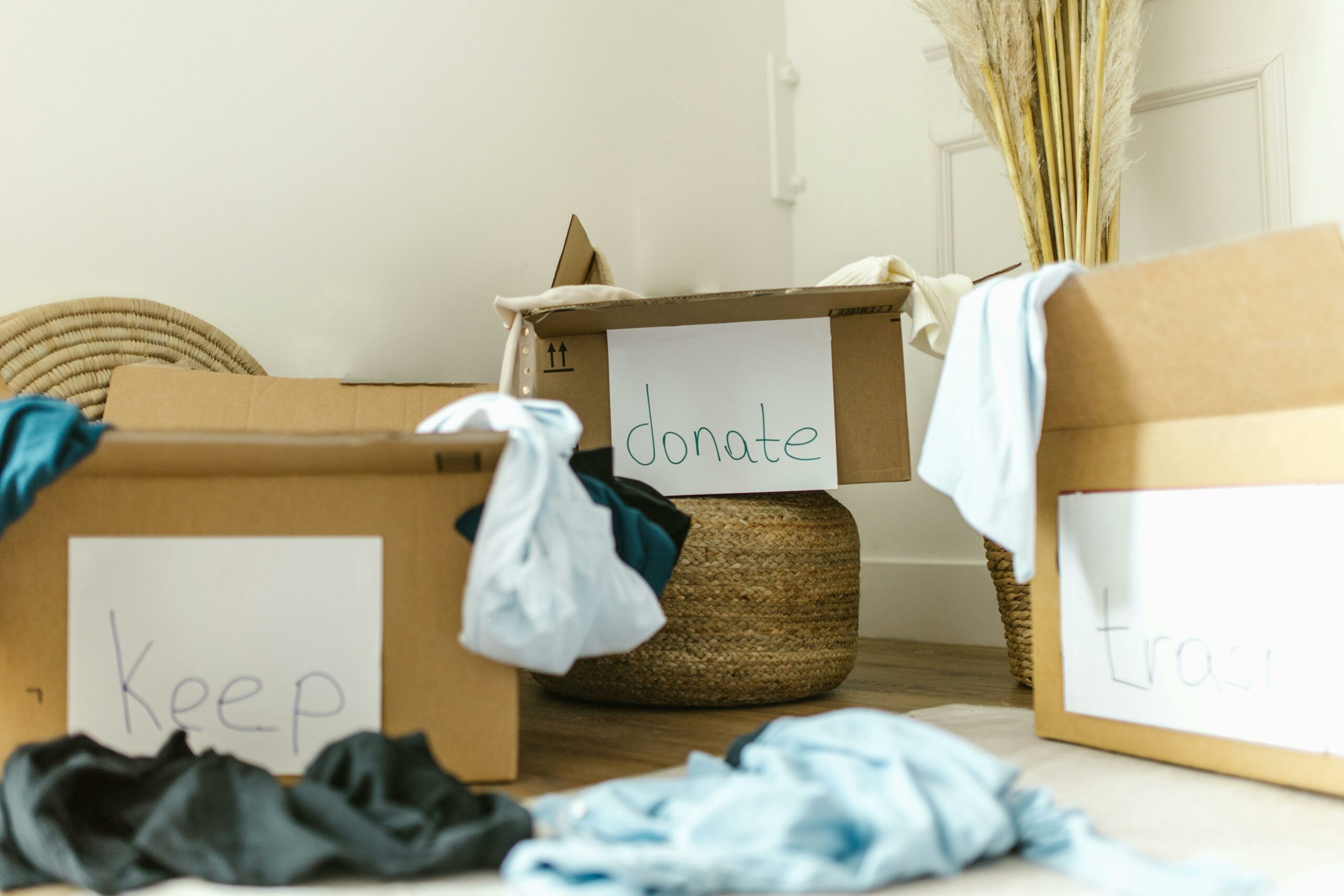 Boxes piled in a room marked keep, donate and trash with clothing inside.